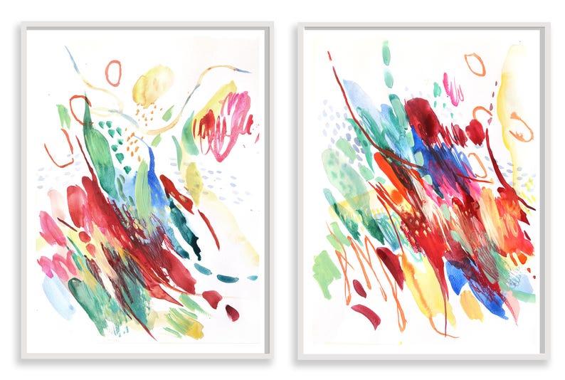 May include: Two framed vertical wall art prints featuring abstract watercolor paintings. The compositions display energetic brushstrokes and splatters in vibrant shades of red, blue, yellow, and green against a clean white background.
