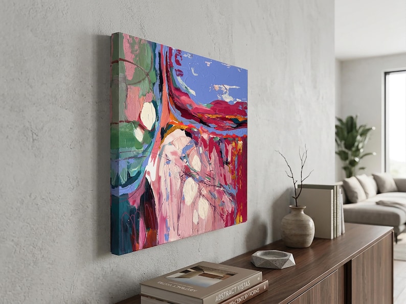 May include: Abstract art canvas with a vibrant mix of colors. The artwork features bold brushstrokes in shades of red, pink, blue, and green. The canvas is mounted on a wooden frame and displayed on a gray wall.
