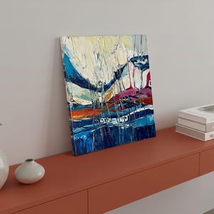 May include: Abstract art canvas with a textured, colorful design. The painting features bold brushstrokes in shades of blue, white, orange, and purple. The artwork is displayed on a red-orange shelf, alongside books and decorative vases.