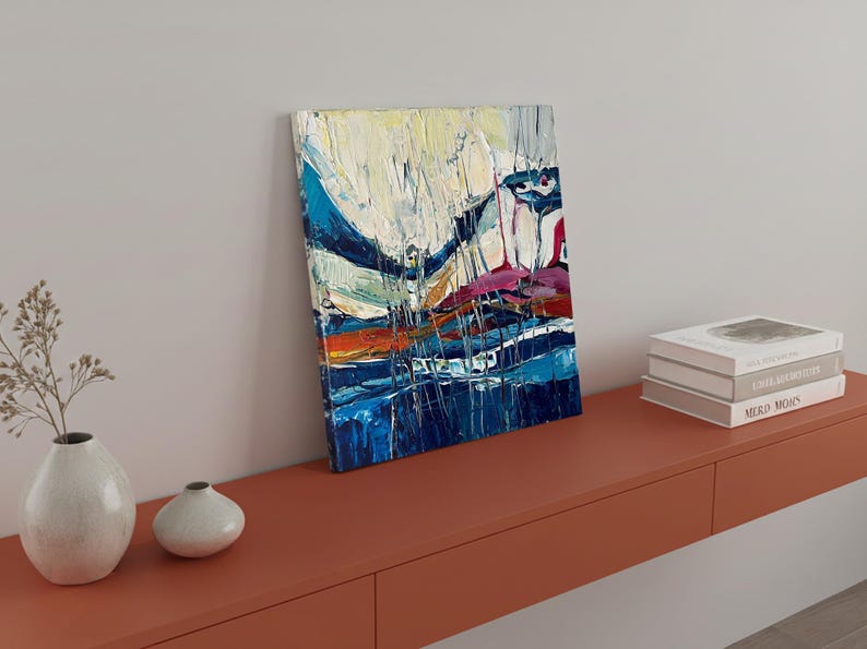 May include: Abstract art canvas with a textured, colorful design. The painting features bold brushstrokes in shades of blue, white, orange, and purple. The artwork is displayed on a red-orange shelf, alongside books and decorative vases.