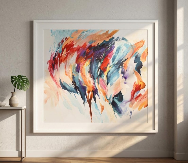 K&ouml;nnte beinhalten: Ein quadratisches gerahmtes Wandbild mit einem abstrakten Gem&auml;lde, das dynamische, schwungvolle Pinselstriche in leuchtenden Rot-, Orange-, Dunkelblau- und Violettt&ouml;nen auf einem hellen cremefarbenen Hintergrund zeigt, in einem schlichten wei&szlig;en Rahmen.