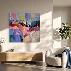 May include: Abstract oil painting with a vibrant colour palette. The artwork features bold brushstrokes in shades of pink, blue, yellow, and red. The painting is displayed on a wall above a wooden cabinet. A modern living room setting with a white chair and a plant.