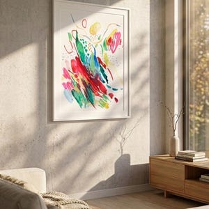 May include: A framed abstract wall art print featuring vibrant, expressive brushstrokes in shades of red, yellow, green, and blue on a white background. The artwork is displayed in a simple white frame, showcasing dynamic, gestural marks and colorful shapes.