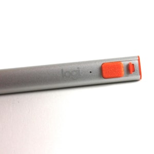 May include: A silver stylus with the word "logi" printed on the side. The stylus has an orange button and a small orange accent on the end. The stylus is designed for use with a tablet or touchscreen device.