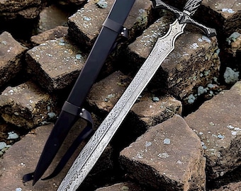 May include: A detailed image of a decorative sword with a patterned blade and ornate hilt. The sword is displayed with its black sheath, resting on a bed of rough, gray rocks. The blade has a unique, textured design.