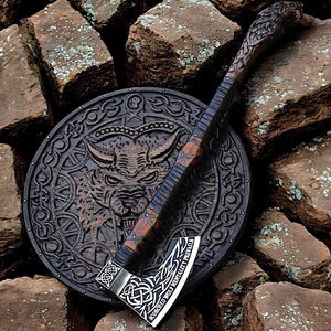 May include: A handcrafted Viking axe and shield set. The axe features a wooden handle with intricate carvings and a metal blade with the text "Scorched Wolf Mentality Prevails." The shield is round, made of wood, and has a carved wolf design.