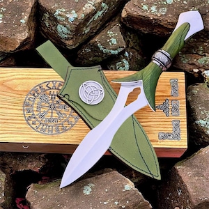 May include: A silver and green dagger with a matching green leather sheath and wooden box. The dagger has a curved blade and a green handle with silver accents. The sheath features a silver emblem. The wooden box has engraved symbols.