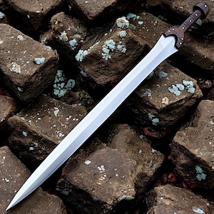 May include: A silver sword with a wooden handle and guard rests on brown stones. The sword's blade is long and sharp, reflecting light. The handle is dark brown, and the guard is a lighter brown. The stones have patches of blue-green lichen.