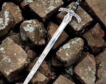 May include: A silver sword with a decorative hilt and blade, resting on a pile of brown bricks. The hilt features black and gold accents, and a red gem is set at the pommel. The blade has an intricate design.