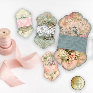 Op de afbeelding: Vijf decoratieve lintrollen met bloemen- en kantmotieven. De rollen zijn gemaakt van papier en hebben een vintage uitstraling. De rollen zijn perfect om elke knutselproject een vleugje elegantie te geven.