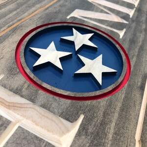 May include: A wooden sign with the word "HOME" carved into it. The sign also features a blue circle with three white stars, representing the state of Tennessee.