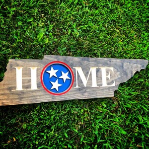 May include: Wooden sign shaped like the state of Tennessee with the word "HOME" in white lettering and a blue circle with three white stars in the centre. The circle has a red outline.