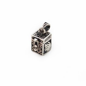 May include: A small, rectangular silver pendant shaped like a box with a hinged lid and a secure latch mechanism. The exterior features intricate dark oxidized scrollwork patterns and a raised, smooth handprint design on the side panel.