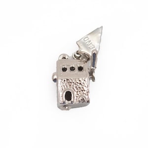 May include: A silver-toned metal charm shaped like a small slot machine with a textured front surface, three circular windows, and a lever on the side. The lever features the word END engraved on its surface, and the charm has a small loop at the top.