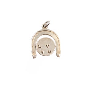 May include: A silver-toned metal charm featuring a horseshoe frame with a circular spinning center. The circular disc is engraved with the letters L, V, Y, and U arranged in a square pattern. A small jump ring is attached to the top of the horseshoe.