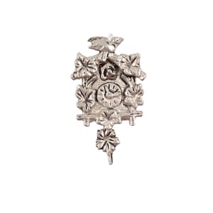 May include: A silver-colored miniature cuckoo clock pendant. The clock features a bird on top, a circular clock face, and decorative leaf and floral accents. The pendulum is a leaf-shaped design. The clock is a detailed, small-scale replica.