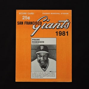 May include: An orange San Francisco Giants 1981 scorecard featuring Frank Robinson, the team's manager. The scorecard includes the text "SCORE CARD" and "PHOENIX MUNICIPAL STADIUM". A black and white photo of Frank Robinson is also included.