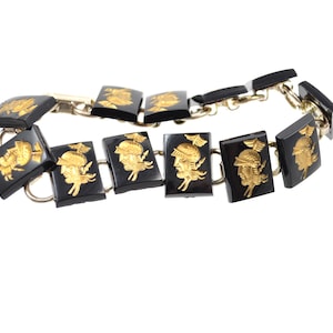 May include: A vintage bracelet featuring rectangular black panels with gold-colored relief portraits. The panels are linked by silver-toned metal. The portraits depict a classical figure with a helmet and wings.