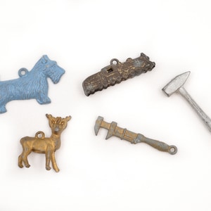 May include: A collection of small, vintage metal charms in various shapes. Includes a light blue terrier, a gold deer, a train, a hammer, and an adjustable wrench. Each charm has a small loop for attaching to a chain or bracelet.