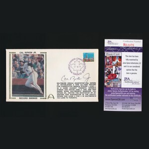 May include: A collectible item featuring a baseball card with a photo of Cal Ripken Jr. in action, a Canadian stamp, and a JSA authentication certificate. The card commemorates a record for consecutive innings played.