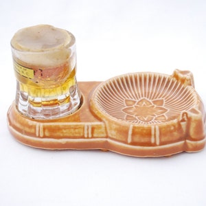 May include: A vintage ceramic beer stein and ashtray set. The stein is clear glass with a foamy top, and the ashtray is brown with a floral design. The set is likely from the mid-20th century.