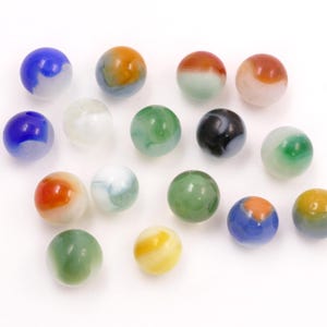 May include: A collection of colorful glass marbles in various sizes and designs. The marbles feature a mix of colors, including blue, green, orange, yellow, and black, with swirling patterns. The marbles are on a white background.