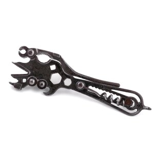 May include: A dark gray metal multi-tool featuring a variety of integrated functions including a corkscrew, a bottle opener, a small wrench, and several serrated edges. The tool has a textured, industrial finish with multiple pivot points.
