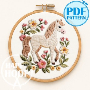 May include: Embroidered horse design in a wooden hoop. The horse is white with a tan mane and tail, surrounded by pink, yellow, and white flowers with green leaves. The text "PDF PATTERN" is in a blue circle.