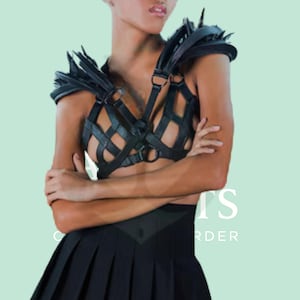 Puede incluir: Armadura de hombro de cuero negro con detalles puntiagudos y un corpiño en forma de jaula. La parte superior se combina con una falda plisada negra, creando una estética audaz y vanguardista. El diseño presenta detalles intrincados y una silueta única.