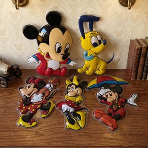 Peut inclure: Un ensemble de cinq plaques murales en plastique coloré représentant des personnages de dessins animés. Le lot comprend un grand Mickey Mouse, un Pluto jaune, une Minnie Mouse jouant de la guitare, une Minnie en robe jaune et un Mickey avec un parapluie.