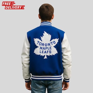 May include: A blue and white varsity jacket with the Toronto Maple Leafs logo on the back. The jacket has white sleeves and a blue body with white stripes on the collar and cuffs. The logo is a white maple leaf with the team name.