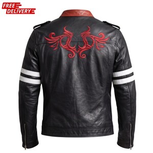 Pode incluir: Um casaco de couro preto com um design tribal bordado a vermelho na parte superior das costas, uma gola de couro castanha e duas riscas brancas horizontais em cada manga. O casaco inclui presilhas nos ombros e fechos prateados nos punhos.
