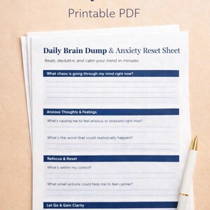 Op de afbeelding: Een stapel afdrukbare PDF-vellen met de titel "Daily Brain Dump & Anxiety Reset Sheet". De vellen bevatten prompts voor reflectie, met een witte en gouden pen die aan de zijkant rust. De bovenste tekst luidt "Daily Brain Dump & Anxiety Reset Sheet Printable PDF."