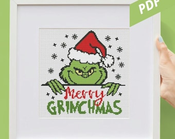 May include: Cross-stitch art of the Grinch wearing a Santa hat, with the text "Merry Grinchmas" in red and green. The artwork is framed in a white square frame.