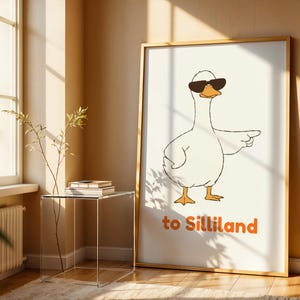 Pode incluir: Uma impressão emoldurada com um desenho de um ganso de desenho animado usando óculos de sol e apontando. O ganso é branco com pés e bico laranja. O texto "to Silliland" é impresso em laranja. A moldura é de cor de madeira clara.