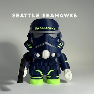 May include: A navy blue and neon green figurine of a Stormtrooper with the Seattle Seahawks logo on the helmet and chest. The figurine is holding a black blaster and has white hands and teeth. The words "SEATTLE SEAHAWKS" are above the figurine.