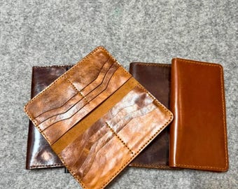 May include: Four leather wallets in shades of brown, from dark to light. The open wallet in the front reveals card slots. The wallets are arranged on a gray surface.