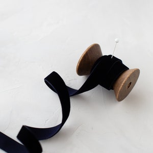 Puede incluir: Un carrete de cinta de terciopelo azul marino con un carrete de madera y un alfiler blanco.