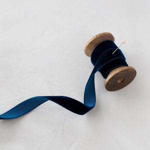 Puede incluir: Un carrete de cinta de terciopelo azul oscuro con un carrete de madera y un alfiler.