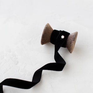 Puede incluir: Un carrete de madera con cinta de terciopelo negro que se desenrolla. La cinta es de color negro oscuro y está sobre una superficie blanca.