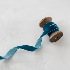 May include: A spool of teal blue velvet ribbon on a wooden spool with a pin.