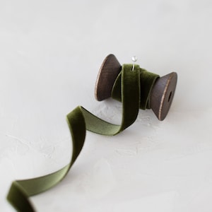 May include: A spool of dark green velvet ribbon with a wooden spool and a pin holding the ribbon in place.