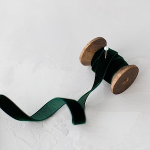 Puede incluir: Un carrete de cinta de terciopelo verde oscuro con un carrete de madera y un alfiler blanco.