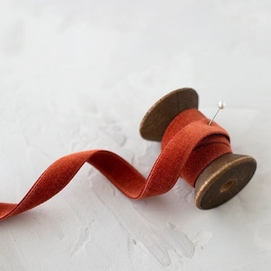 May include: A spool of burnt orange velvet ribbon with a wooden spool and a pin holding the ribbon in place.