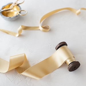 May include: A spool of gold satin ribbon with a wooden spool and a pair of gold scissors in a small grey bowl.