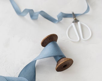 Puede incluir: Un carrete de cinta azul claro con un carrete de madera y un pequeño par de tijeras plateadas sobre un fondo blanco.