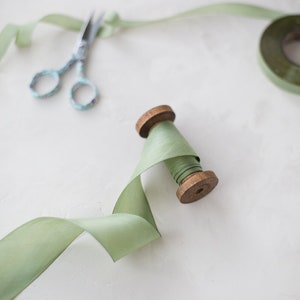 May include: A spool of sage green ribbon with a wooden spool and a pair of silver scissors.