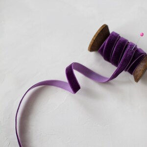 May include: A spool of purple velvet ribbon with a wooden spool and a pink pin.