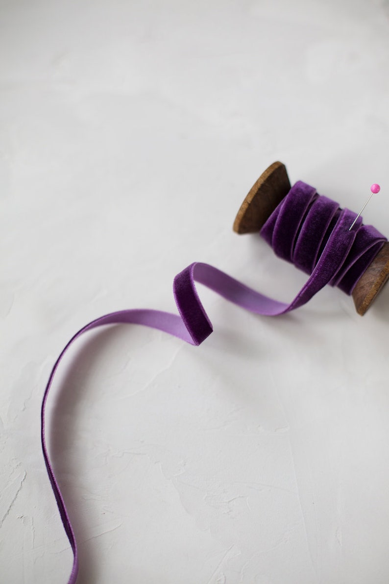May include: A spool of purple velvet ribbon with a wooden spool and a pink pin.