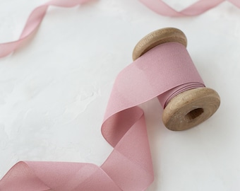 May include: A spool of dusty rose pink ribbon with a wooden spool. The ribbon is soft and delicate, perfect for adding a touch of elegance to any project.